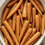 Maple glazed roasted carrots on a baking sheet, brushed with melted butter and maple syrup, sprinkled with fresh thyme — a sweet and savory fall side dish perfect for holidays or weeknight dinners.